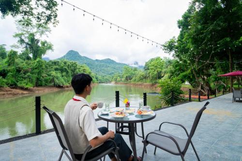 a man sitting at a table with a view of a river at Puprai Tarnnarm Resort in Thong Pha Phum