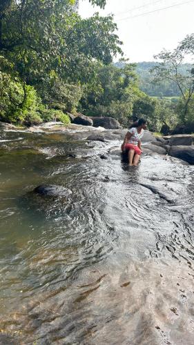 a woman sitting on a rock in a river at Doddakallu Betta Homestay Coorg in Somvārpet