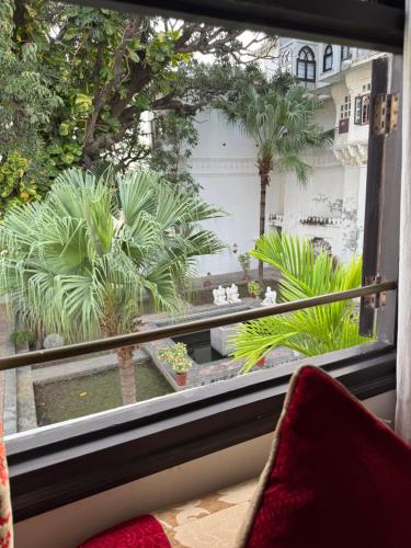 a window with a view of a garden with palm trees at Amet Haveli - A Heritage Hotel Udaipur in Udaipur