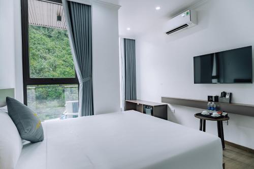 a white bedroom with a bed and a tv at Sand Hotel in Cat Ba