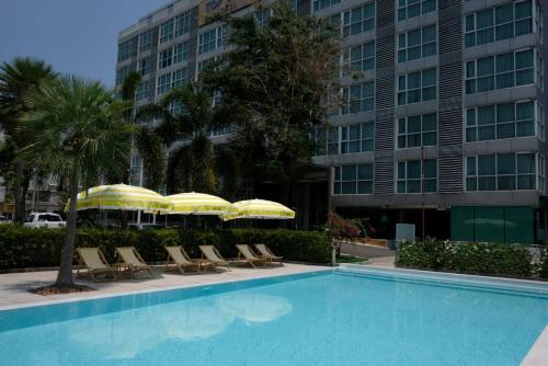 a swimming pool with chairs and umbrellas in front of a building at Top View Hotel - SHA Extra Plus in Si Racha