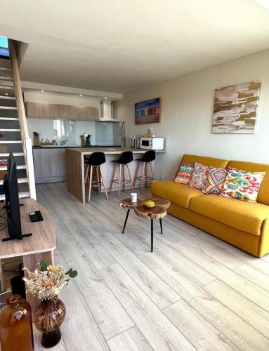 un salon avec un canapé jaune et une cuisine dans l'établissement Le rêve bleu de Jeanne et Marie-vue mer, à Cucq