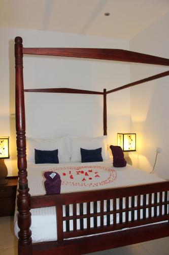 Cama de madera con dosel, sábanas blancas y almohadas azules en Villa Kapuru en Negombo