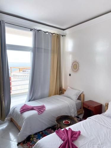 a bedroom with two beds and a window with a balcony at Locals Taghazout surfcamp in Taghazout