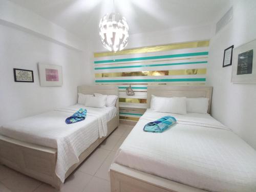 グアヤカネスにあるLas Olas, Juan Dolio 2bed2bath Condoの白い壁とシャンデリアが特徴の客室で、ベッド2台が備わります。