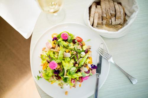 a salad on a white plate with a fork and a bowl of bread at Hotel de Blanke Top in Cadzand-Bad