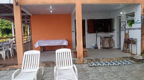 2 weiße Stühle und ein Tisch auf einer Veranda in der Unterkunft Casa 5 quartos Ilha de Itacuruça RJ in Mangaratiba