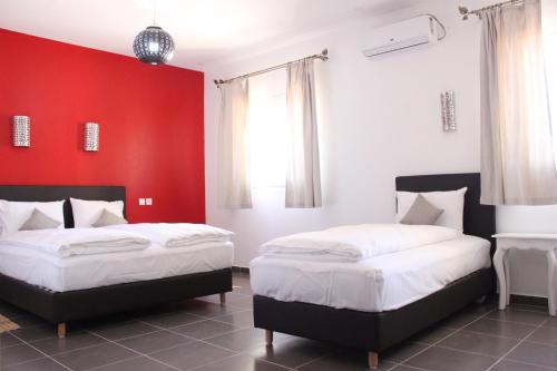 two beds in a room with a red wall at Auberge Tinit in Er Rachidia