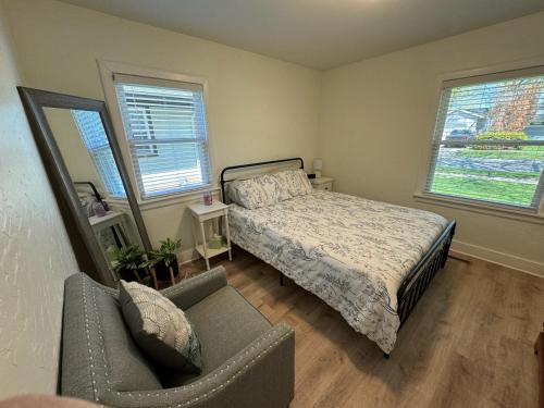 a bedroom with a bed and a chair and two windows at Cozy Neutral Farmhouse, Coffee provided, Relaxation optional in Muskegon