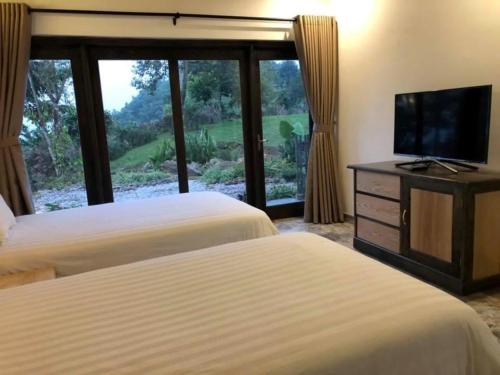 two beds in a room with a tv and a window at Bakhan Village Resort in Mai Chau