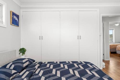a bedroom with a blue and white bed and white cabinets at Pacific Breeze in Caves Beach