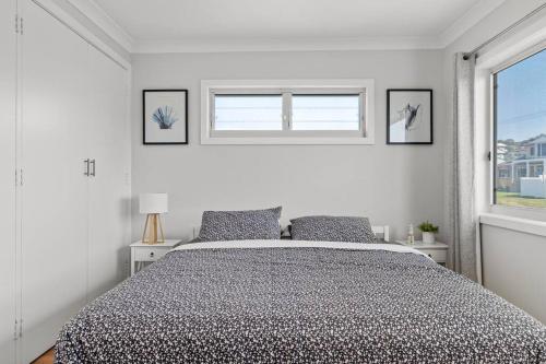 a white bedroom with a bed and two windows at Pacific Breeze in Caves Beach