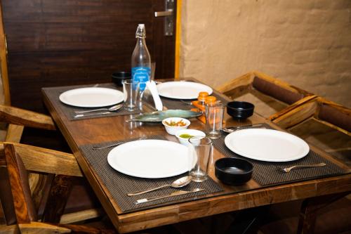 a wooden table with white plates and utensils on it at Maatidera Resort Kanatal The Boutique stay in the Lap of Himalayas in Kanatal