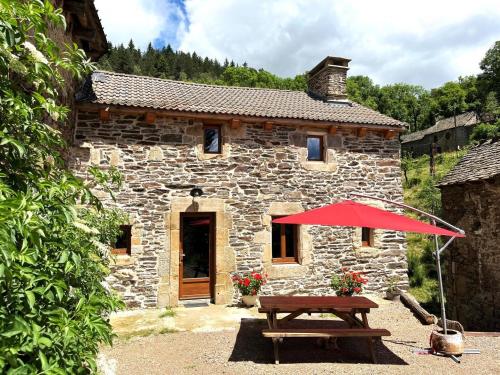 a stone house with a picnic table and a red umbrella at Gite de montredon in Cubières