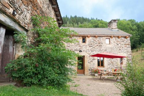 a stone house with a table and a red umbrella at Gite de montredon in Cubières