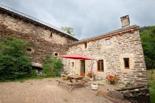 a stone building with a picnic table with a red umbrella at Gite de montredon in Cubières