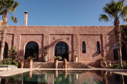 a building with a swimming pool and palm trees at Le Jardin des Douars in Ghazoua