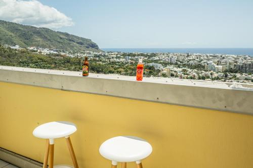 two stools on a balcony with a view of a city at Le Doux Bleu Vue - Vue mer & montagne - Wiskeys in Saint-Denis