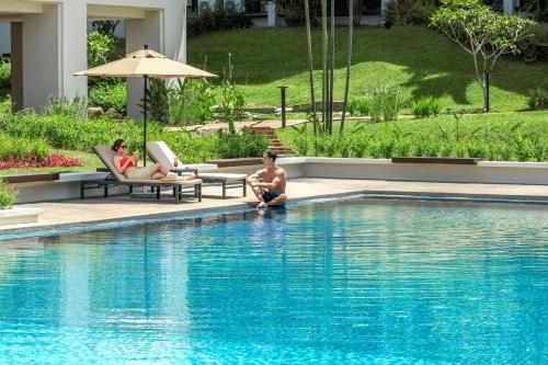two people sitting in chairs next to a swimming pool at Palm Garden Hotel, Putrajaya, a Tribute Portfolio Hotel in Putrajaya