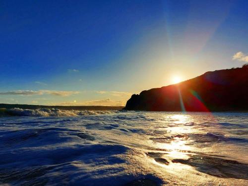 a beach with the sun setting on a mountain at Clyne Farm Centre in The Mumbles