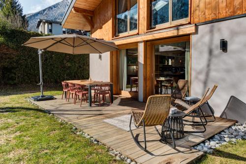 une terrasse en bois avec une table, des chaises et un parasol dans l'établissement Chalet Arve - Alpes Travel - Chamonix - Sleeps 10, à Chamonix-Mont-Blanc