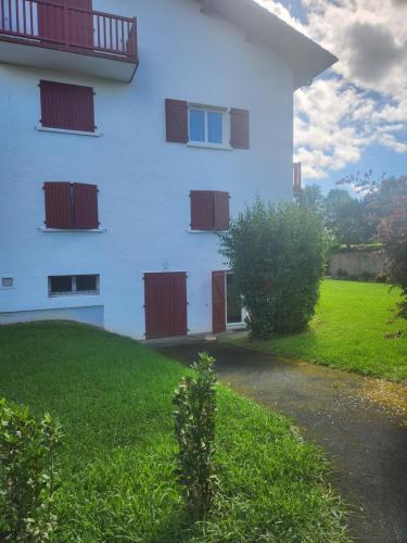 un bâtiment blanc avec des portes rouges et un champ vert dans l'établissement Studio sur les fleuristes, à Cambo-les-Bains