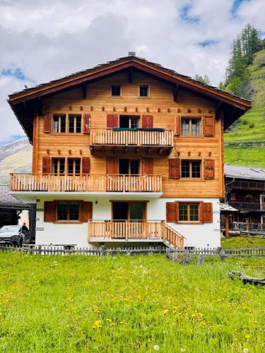 a large wooden house with a balcony on a green field at Appartement spacieux in Haudères