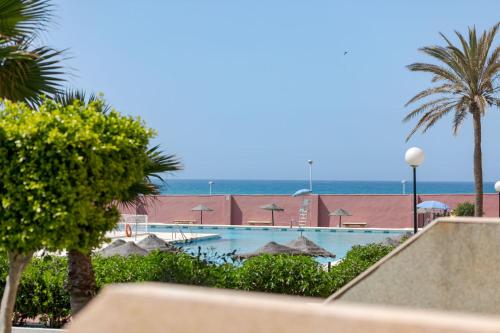a view of a swimming pool with palm trees and the ocean at BAJO primera línea playa, Retamar, Cabo de Gata in Retamar