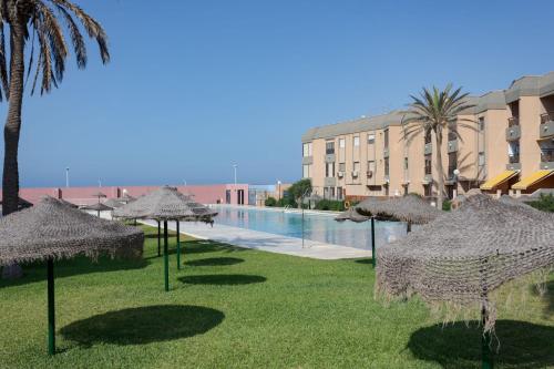 a group of straw umbrellas in the grass near a pool at BAJO primera línea playa, Retamar, Cabo de Gata in Retamar