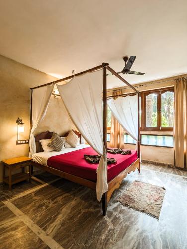 a bedroom with a canopy bed with red sheets at Nalanda Retreat Goa By Mandrem Beach in Mandrem