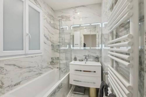 La salle de bains blanche est pourvue d'un lavabo, d'une baignoire et d'un miroir. dans l'établissement Luxe à la francaise 75017, à Paris