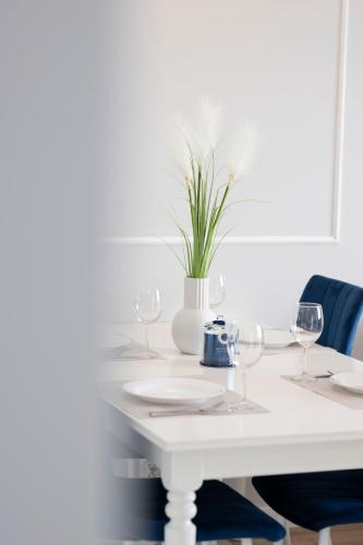 a white table with glasses and a vase with a plant at Apartament Glamour in Gdańsk