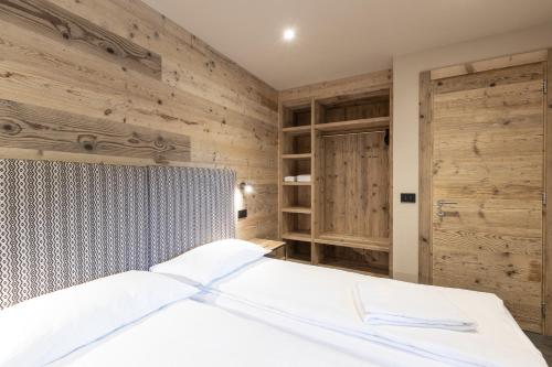 a bedroom with a white bed with wooden walls at BAITA LARIX BORMIO in Bormio