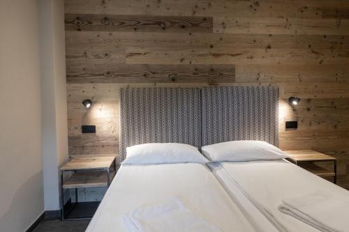 a bedroom with a white bed with a wooden wall at BAITA LARIX BORMIO in Bormio