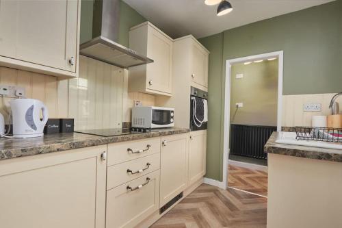 a large kitchen with white cabinets and a microwave at Cosy 3-Bedroom House in Seaham - Street Parking in Seaham