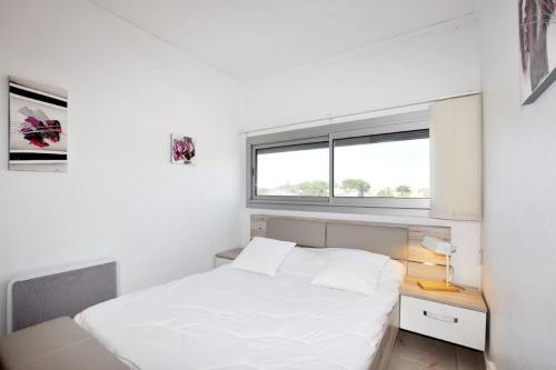 une chambre avec un lit blanc et une fenêtre dans l'établissement Oasis rénovée, plage, 2 parkings, wifi au Barcarès, au Barcarès