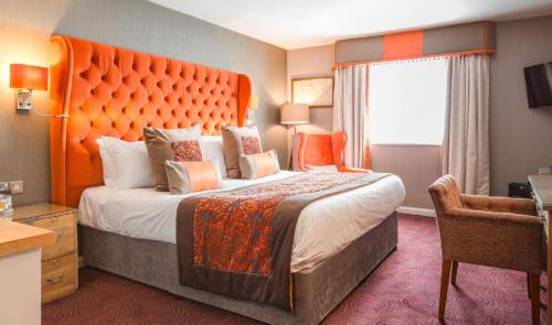 a hotel room with a large bed with an orange headboard at Thornton Hall Hotel & Spa in Heswall
