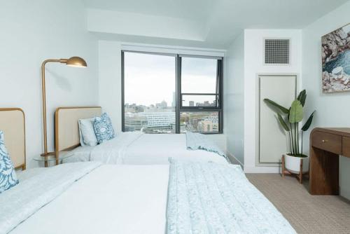 a white bedroom with two beds and a window at Central Square Penthouse near MIT Harvard Wi-Fi & GYM in Cambridge