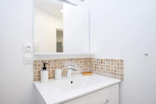 une salle de bain blanche avec un lavabo et un miroir dans l'établissement Ma petite Folie Appt 3 pers porte du jerzual, à Dinan