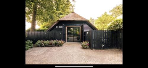 a small black building with a door and flowers at Luxe Hofstede met paardenstalling in Lunteren