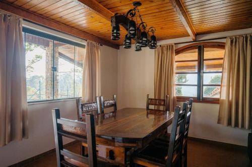 a dining room with a wooden table and some windows at Pousada das Pedras in Monte Verde