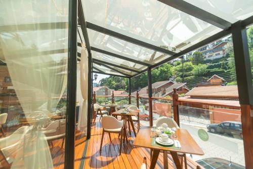 a glass house with a balcony with tables and chairs at Pousada Santa Felicidade in Campos do Jordão