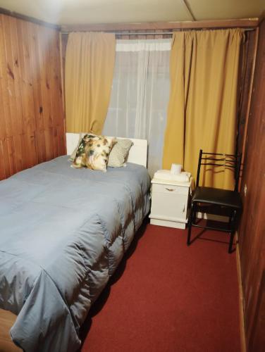a bedroom with a bed and a chair and a window at Pensión San Andrés in Concepción