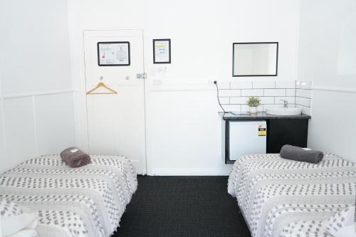 two beds in a white room with a sink at Queensland Hotel in Goondiwindi
