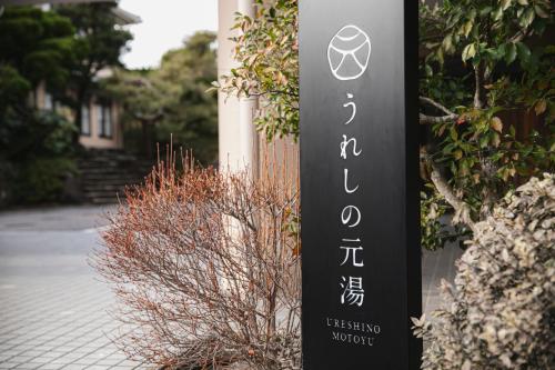 a sign for a hotel next to a bush at Ureshino Motoyu in Ureshino