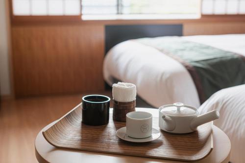 a wooden tray with two cups and towels on a bed at Ureshino Motoyu in Ureshino