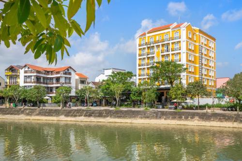 a tall yellow building next to a body of water at Royal Riverside Hoi An Hotel & Spa in Hoi An