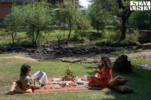 two girls sitting on a picnic blanket in the grass at StayVista at Swiss Chalet - Tangmarg with Gazebo & Lawn in Tangmarg
