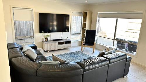 a living room with a leather couch and a flat screen tv at Coastal Oasis - 10 mins to Torquay, 10 mins to Geelong ! in Mount Duneed
