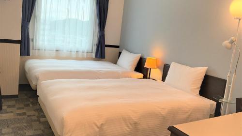two beds in a hotel room with a window at Toyoko Inn Niihama Ekimae in Niihama